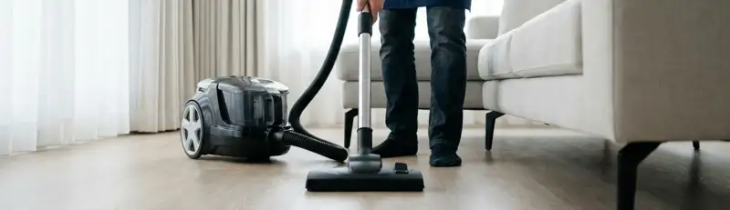 Professional house cleaner vacuuming a living room floor with a canister vacuum cleaner, Dallas, TX.