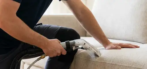Professional upholstery cleaner deep-cleaning a fabric sofa with a handheld extraction tool, Dallas, TX.