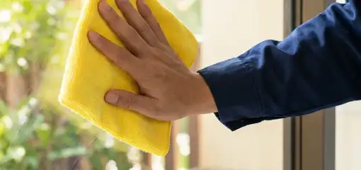 House cleaner wiping a glass window with a yellow microfiber cloth for streak-free cleaning, Dallas, TX.